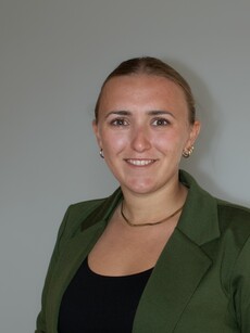 Porträt einer Person in grüner Jacke vor grauem Hintergrund; Gesicht unkenntlich gemacht.